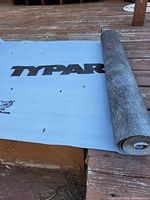 Partial unrolled Typar branded gray woven fabric roll on wooden surface.