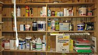 Shelving unit with assorted building and cleaning supplies including chemical bottles, containers, cans, and boxes.