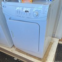 Front view of white Maytag dryer with control panel and door handle, placed on a wooden platform.