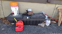 Photo showing exterior of black plastic storage box with buckets stacked on top, red gas can and other containers beside it