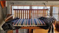 Front view of wooden porch swing with striped cushion covered partly in protective plastic.