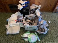 View of all assorted silver plate items, coffee urn in box, window sheers, craft items, and laundry hampers arranged on a carpet.