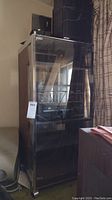 Full view of the tall wooden cabinet with glass front door housing the stereo components and speakers stacked on top