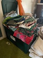 Large green storage bin filled with folded tablecloths of various colors and patterns.