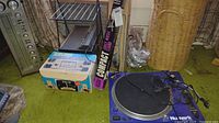 Photo showing Numark TT1700 turntable on green carpet next to a boxed vintage slide/movie screen and foldable music stand.
