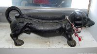 Side view of the cast-iron dachshund doorstop showing dog's elongated body, curled tail, and braided cord.