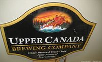 Front view of the curved tin advertising sign featuring an illustration of men in a canoe and text branding Upper Canada Brewing Company.