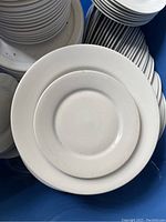 Close-up photo of a large white plate showing smooth, plain white ceramic surface and round shape with a slightly raised rim.