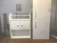 Photo of two white wall-mounted bathroom storage units, a tall cabinet with doors and a smaller shelf unit with drawers and open shelves.