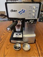 Front view of Oster espresso machine with portafilter and two metal baskets on drip tray