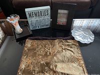 Photo of assorted decorative items staged on a glass coffee table including a glass ruffled vase, framed sign, decorative fabric, box, and glass dish.
