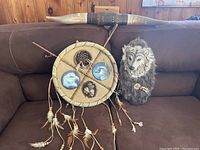 Full view of three Indigenous art pieces on brown couch: long horn, dreamcatcher, wolf head mount.