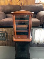 Front view of closed wooden jewelry box with glass door on black surface.