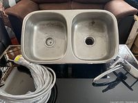 Photo of double stainless steel kitchen sink with two basins and drain openings. Sink shows light surface wear.