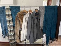 Three ladies coats and six scarves hanging on a rack, showing variety of coats and scarf textures and colors.