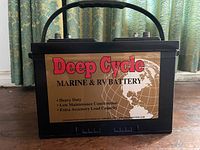 Front view of black Deep Cycle marine and RV battery showing label with construction and load capacity details.