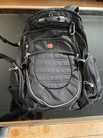 Front view of the Swiss Army black backpack showing the logo, multiple zippered compartments, and carry handle.