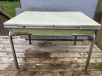 Full front view of the vintage 1950s Formica table showing green patterned top and rusted chrome legs with yellow leg caps.