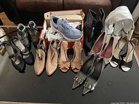 Wide shot showing the entire lot of women's footwear on a black table, displaying all different types and colors of shoes and boots including the Nike runners in the box.