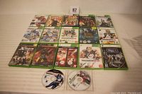 Photo showing 17 Xbox and Xbox 360 game cases arranged in rows, visible titles including Madden NFL series, Fallout New Vegas, Rainbow Six Vegas, Halo 2, Assassin's Creed II, and others.