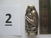 Front view of a silver/nickel plated match safe shaped like a monkey smoking a long pipe with detailed fur and facial features, placed beside a ruler showing height just under 3 inches.