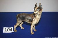 Full side view of the cast iron Boston Terrier doorstop on blue cloth background with lot number 104.