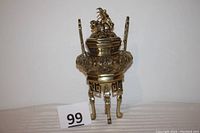 Front view of brass urn showing dragon on lid, tripod legs, and ornate detailing.