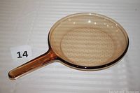 Top view of amber glass frying pan with handle and smooth rim on white surface.