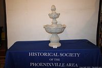 Full view of the two-tier concrete garden water fountain on a blue covered table.