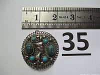 Front view of round pendant with turquoise stones, scarabs, and Nefertiti figure showing detailed front design and size relative to ruler.