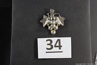Front view of vintage silver brooch shaped as grape cluster with leaves on a black background.