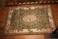 Full view of the rectangular rug showing the sage green center, floral ivory oval medallion, and the ivory floral border on wood floor.