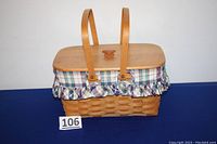Front view of assembled Longaberger rectangular picnic basket with dual wooden handles, plaid cloth liner, and fitted wooden lid on top.