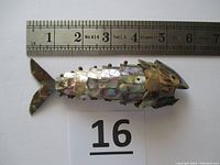 Top view of shellfish sculpture with measuring ruler showing 5.75 inches length, displaying layered abalone shells and metal articulation points.