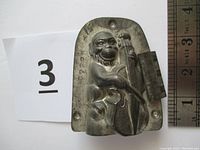 Front view of tin chocolate mold showing detailed monkey holding bass fiddle with ruler for size reference.