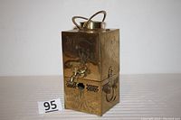 Full front view showing spigot, engraved landscape and figure designs, hinged lid with handle.