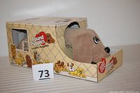 Front angled view of the plush Mom Pound Puppy inside the original cardboard doghouse box, showing the dog partially sticking out and box branding