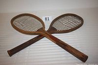 Two vintage wooden tennis rackets shown crossed, revealing wooden frames and string wear.