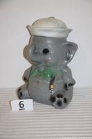 Front and side view of the vintage chalkware elephant coin bank with white hat, green bow tie, and gray body.