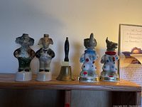 Image shows four ceramic animal decanters and one brass bell on a wooden shelf.