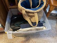 Clear plastic bin filled with various bags including woven tote, black bag, and fabric organizers