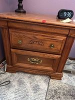 Front view of one Broyhill bedside table showing two drawers, a digital clock, and a lamp on top, with visible wood grain and brass drawer pulls.