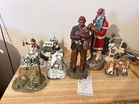 10 Christmas figurines and houses arranged on a wooden surface showing all items together.