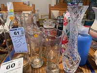 Several clear glass vases, a floral-patterned pitcher, and glass cups shown on a wooden dining table.