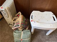 Full lot showing Cuori heater, quilt in packaging, green throw blanket, and white shower chair on carpet.