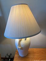 Full view of one lamp showing white textured pottery base with rope and cream pleated shade with grey trim