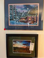 Two framed and matted signed original art prints by C. Hodges hung on a wall, showing the winter night scene above and the sunset scene below.