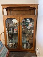 Full front view of oak China cabinet showing glass doors and wood design details with contents inside.