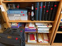 Shelf with multiple large black and blue photo albums, plastic storage totes, holiday card boxes, stationery items, and a black bag in the foreground.