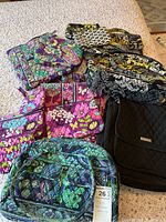 Overall group photo showing 14 Vera Bradley purses and bags in multiple patterns including floral and paisley in colors pink, green, blue, black, and yellow on a fabric surface.